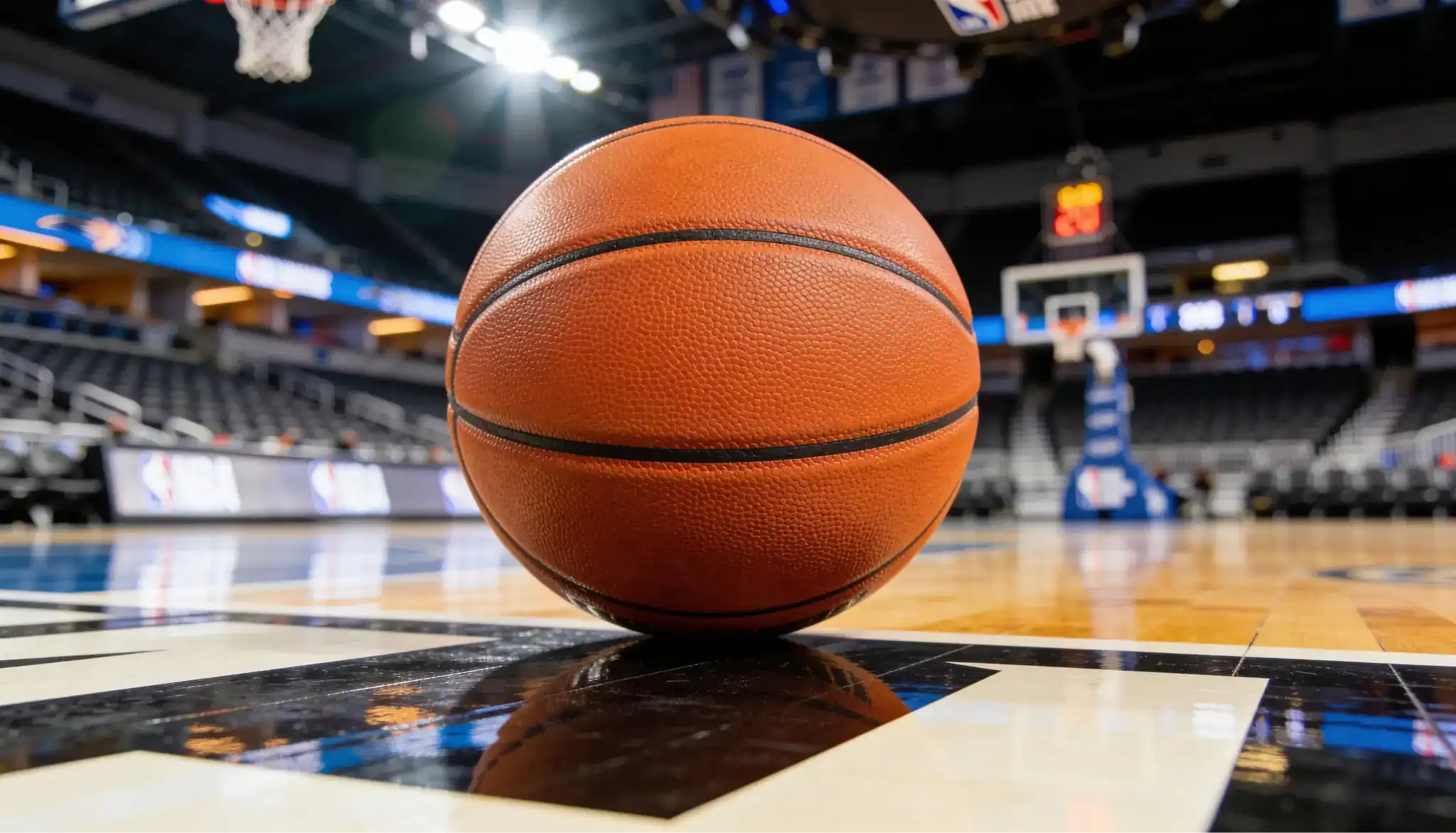 Basketball on hardwood court with arena seating in background